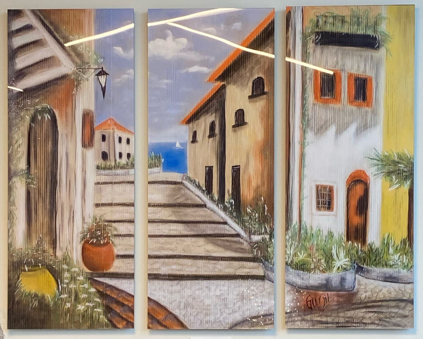 A limited edition acrylic gloss triptych print featuring a painting of an Italian street scene with cobblestone pathways, buildings, and a blue sky. Triptych.